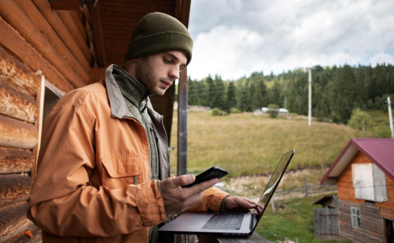 man outside rural cabin trying to use full fibre broadband on his laptop and phone