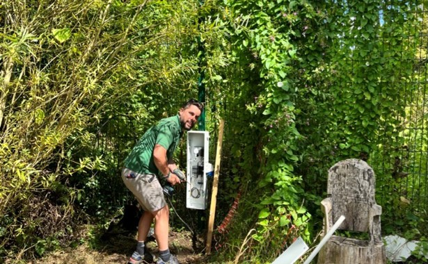 Employee installing a wildlife camera to a fence
